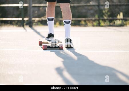 Rückansicht von männlichen Hipster Reiten Longboard entlang Asphaltstraße An sonnigen Tag im städtischen Bereich Stockfoto