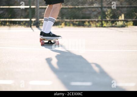 Rückansicht von männlichen Hipster Reiten Longboard entlang Asphaltstraße An sonnigen Tag im städtischen Bereich Stockfoto