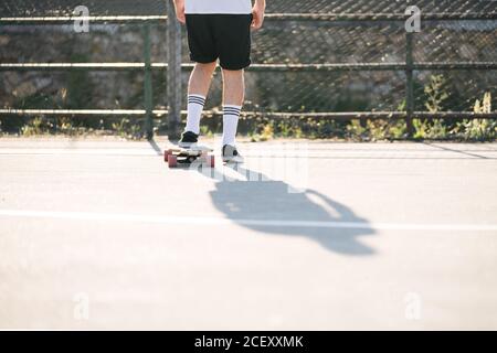 Rückansicht von männlichen Hipster Reiten Longboard entlang Asphaltstraße An sonnigen Tag im städtischen Bereich Stockfoto