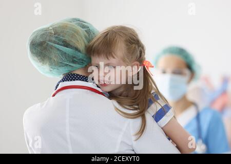 Doktor steht mit dem Rücken und hält sich in den Armen Kleines verängstigtes Mädchen Stockfoto