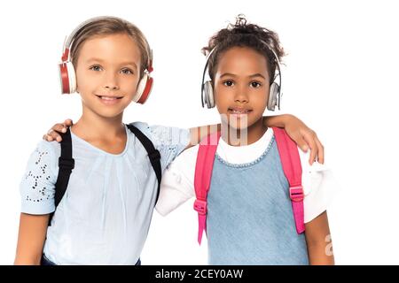 Multikulturelle Schüler hören Musik in kabellosen Kopfhörern, während sie sich die Musik anschauen Kamera auf Weiß isoliert Stockfoto