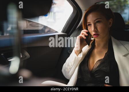 Beschäftigte Unternehmerin sitzt in Luxus-Auto sprechen auf mobilen Telefon funktioniert Stockfoto