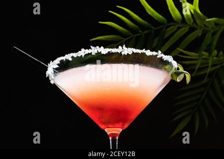 Tropischer Margarita Cocktail mit Grenadine auf glitzerndem Tisch platziert mit Pflanzenblätter auf schwarzem Hintergrund Stockfoto