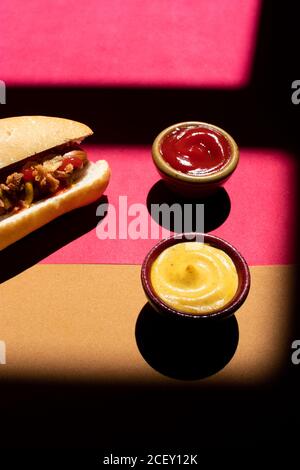 Von oben frankfurter Hot Dog mit Senf und Ketchup serviert Auf kleinen Schüsseln auf buntem Hintergrund Stockfoto