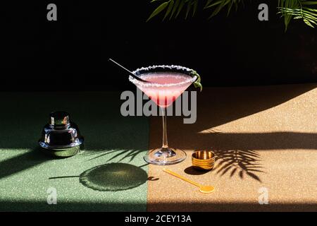 Tropischer Margarita Cocktail mit Grenadine auf glitzerndem Tisch platziert mit Pflanzenblätter auf schwarzem Hintergrund Stockfoto