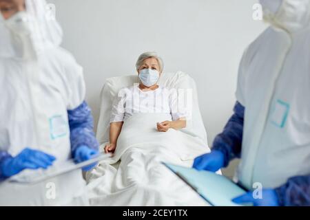 Zwei nicht erkennbare Ärzte stehen auf der Krankenstation mit älteren Frauen Patient im Bett, der etwas diskutiert Stockfoto