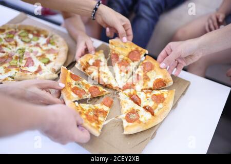 Auf dem Tisch sind zwei offene Boxen Pizza, jeder der bestehenden Menschen nimmt Stück. Stockfoto