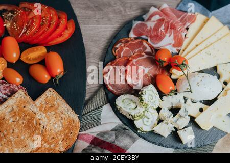 Von oben verschiedene leckere Vorspeisen einschließlich Schinken und sortiert Käse mit frischen Tomaten und Toastbrot auf Holz serviert Tabelle Stockfoto