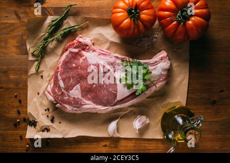 Draufsicht auf rohes Rindfleisch auf Bastelpapier Tisch mit frischen Tomaten und Olivenöl mit Gewürzen angeordnet Und Knoblauch Stockfoto