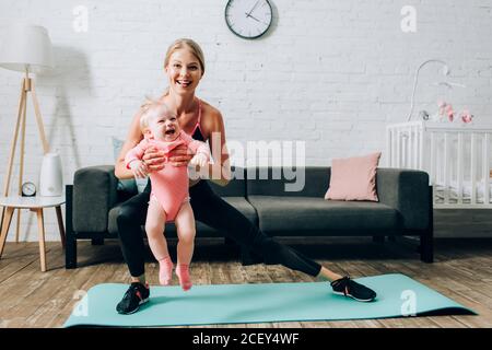 Sportlerin dabei Ausfallschritte auf Fitness-Matte und Tragen Baby Tochter Stockfoto
