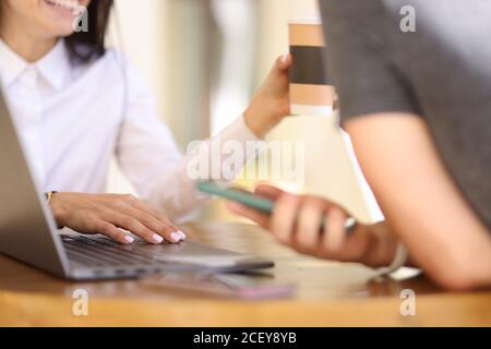 Lächelnde Frau im Café hält Hand auf Laptop-Tastatur als nächstes Zum Mann mit Smartphone Stockfoto