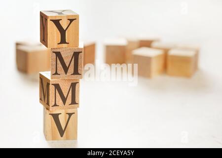 Vier Holzwürfel im Stapel mit Buchstaben YMMV (was bedeutet, dass Ihre Kilometerzahl variieren kann) auf ihnen angeordnet, Platz für Text / Bild in der rechten unteren Ecke Stockfoto