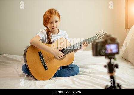 Portrait von schönen niedlichen kaukasischen Kind Mädchen blogger Gitarre spielen bei der Kamera. Liebenswert Mädchen sitzen zeigen, Durchführung neuer Melodie für Abonnenten. vl Stockfoto