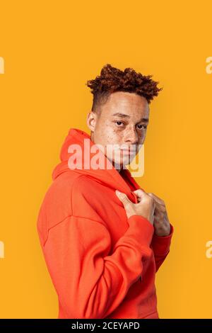 Freistil. Mulatto Kerl im Hoodie stehend isoliert auf gelb posiert Kamera nachdenkliche Seitenansicht Stockfoto