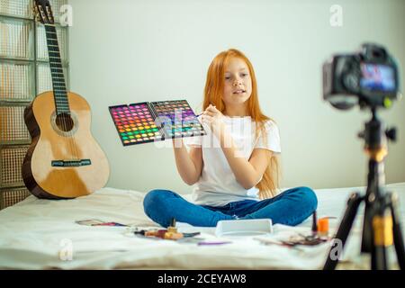 Portrait von kleinen kaukasischen Blogger Kind interessant reden über Kosmetik, nettes Mädchen mit langen roten Haaren präsentieren Schönheit Dinge, sitzen vor der Kamera Stockfoto