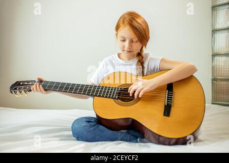 Kleine kaukasische Bloggerin Mädchen spielen Gitarre bei der Kamera. Sie führt Musik. Enthusiastische autodidaktischer Mädchen mit roten Haaren genießen, interessant für subsc Stockfoto