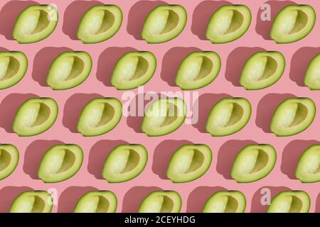 Trending Stil Muster der Hälfte seedless grün Avocado auf rosa Hintergrund mit hartem Licht. Kreative Lebensmitteltextur Stockfoto