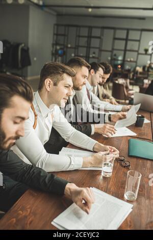 Junge kaukasische Geschäftsleute in formeller Kleidung halten Aufzeichnungen auf Papier, Notizen machen und diskutieren, isoliert in modernen Sitzungssaal Stockfoto