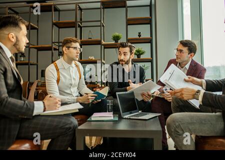 Erfolgreiche und selbstbewusste kaukasische Männer, Geschäftspartner halten Treffen im modernen Büro. Junge Männer in formeller Kleidung diskutieren und Planungsstrategien toge Stockfoto