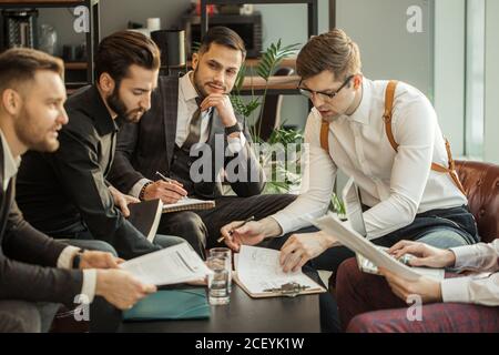 Junge kaukasische Geschäftsleute in formeller Kleidung halten Aufzeichnungen auf Papier, Notizen machen und diskutieren, isoliert in modernen Sitzungssaal Stockfoto