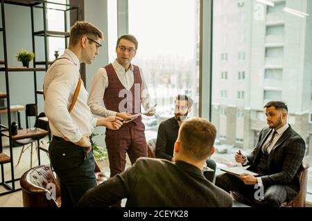 Erfolgreiche und selbstbewusste kaukasische Männer, Geschäftspartner halten Treffen im modernen Büro. Junge Männer in formeller Kleidung diskutieren und Planungsstrategien toge Stockfoto