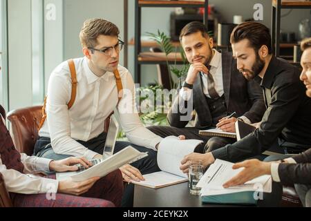 Junge kaukasische Geschäftspartner teilen und kommentieren Berichte. Halten Papiere und Notizbücher, Notizen machen und Aufzeichnungen über ihren Markt, in Form Stockfoto