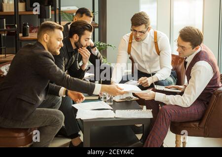 Junge selbstbewusste Männer entwickeln neue Existenzgründung, diskutieren Interaktion in Finanzen und Markt, Austausch von Meinungen und Ideen miteinander, gekleidet Stockfoto