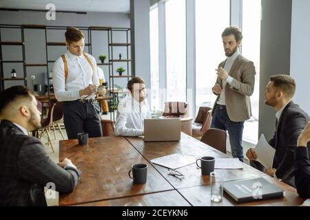 Junge kaukasische Geschäftsleute, gutaussehende Jungs in eleganten stilvollen Tux bei der Sitzung, halten Konferenz für die Diskussion neuer Startup-Business-Projekt. Erfolg Stockfoto