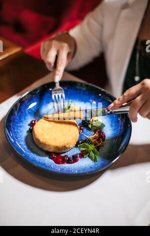 Zarte weibliche Hände halten silberne Gabel und Messer, Schneiden frisch zubereiteten Dessert, schöner Kuchen wird am Tisch in glorreichen dunkelblauen Teller vor serviert Stockfoto