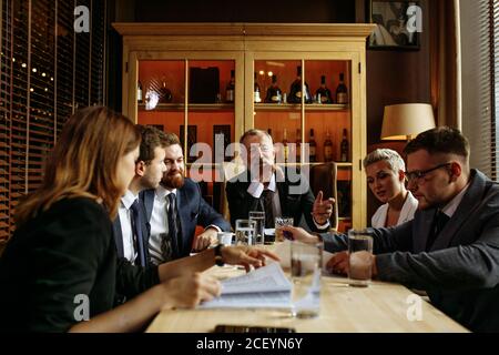 Junge ehrgeizige Menschen sitzen an großen Holztisch in hell Büro und Überlegungen über strategische Pläne für die Geschäftsentwicklungsmodellierung Über der Glaskabine Stockfoto