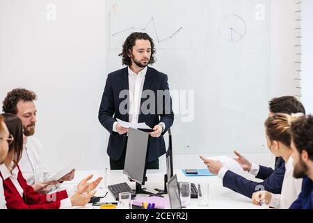 Serious Business man, Chef oder Manager macht eine Präsentation an Kollegen, geben Handouts. Menschen auf dem Tisch sitzen aufmerksam zuhören, um ihn Stockfoto