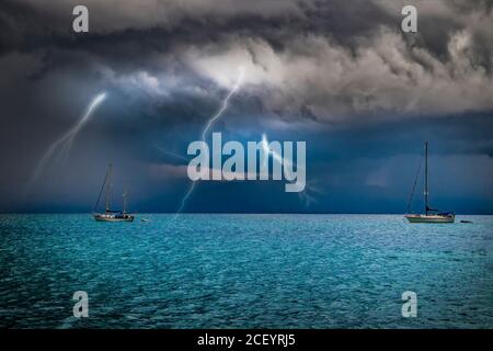 Yachten sind im Sturm auf See. Blitze blitzen vom Himmel ins Wasser. Es ist in Sardinien, Italien. Es regnet von schwarzen Wolken. Stockfoto