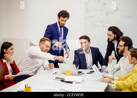 Junge kaukasische Menschen versammelten sich im Büro, um Geschäftsprojekte und Ideen zu diskutieren, tragen formale Kleidung isoliert im modernen Büro. Vielfältig begeistert Stockfoto