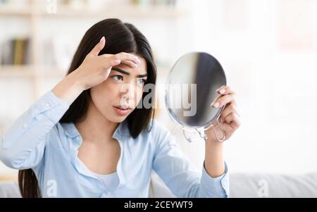 Problemhaut. Sorge Asiatische Frau Suchen In Runden Spiegel Und Berühren Stirn Stockfoto