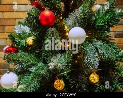 Fragment eines Weihnachtsbaums mit roten und weißen Kugeln Und eine Girlande in Form von Korbbällen mit Eine Glühbirne im Inneren Stockfoto