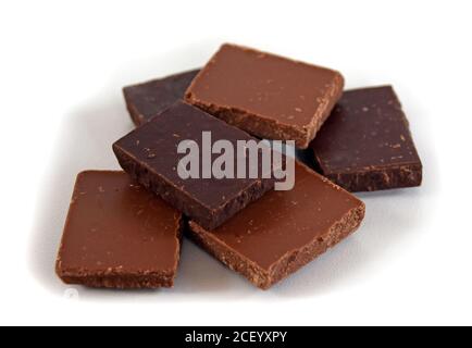 Milch- und dunkle Schokoladenwürfel. Schokoladenstapel auf weißem Hintergrund. Stapel Schokolade. Kleine dunkle Schokoladenstücke. Stockfoto