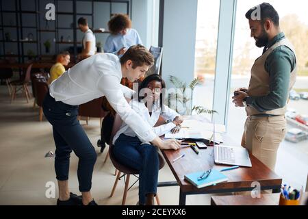 Vielbeschäftigte multiethnische Geschäftsleute, die im Coworking Space zusammenarbeiten, diverse Mitarbeiter, Geschäftsteam, das im Büro zusammenspricht, Projektteam Stockfoto