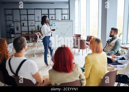 Schwarze Geschäftsfrau Stand sprechen erklären, machen Flipchart-Präsentation für Büroangestellte mit Diagrammen, motivierte afroamerikanische Sprecher Co Stockfoto