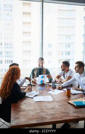 Ein enthusiastisches und ambitioniertes Team von Geschäftsleuten sitzt zusammen auf dem Tisch und diskutiert zukünftige Schritte für die Geschäftsstrategie. Hintergrund des Büros Stockfoto