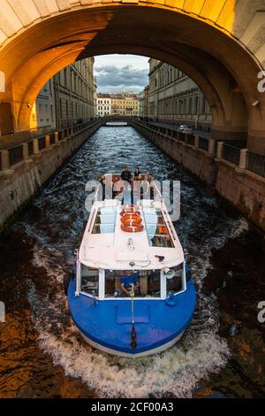 Touristenboot mit Passagieren während der Exkursion im Winterkanal in St. Petersburg in der Nähe der Eremitage am Herbstabend bei Sonnenuntergang. Blick von oben Stockfoto