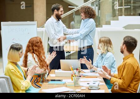 Verwirrt großer Mann mit Afro Frisur gekleidet formell hellblaues Hemd hält die Hand des zufriedenen Chef, gibt Handschlag mit rätselhaften Gefühlen in modern Stockfoto