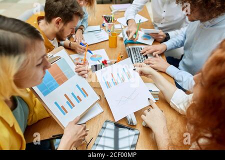 Arbeitsprozess der jungen positiven Team von Grafikdesignern, lässig gekleidet, sitzen am Tisch, diskutieren Design-Projekte, machen Desisionen, High-Angle-Ansicht Stockfoto