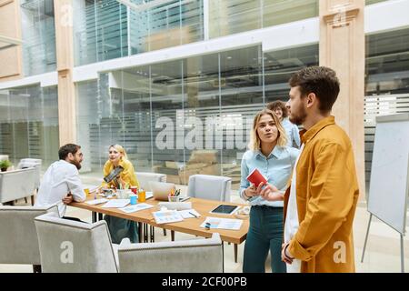 Ziemlich charmante Mädchen mit langen blonden Haaren, trägt Jeans und hellblaues T-Shirt, spricht mit schönen Kerl in lässigem Outfit, schaut weg mit offenem Mund, te Stockfoto