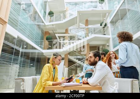 Bottom shot von Geschäftspartnern sitzen am Tisch, junge blonde Dame konzentriert sich auf Laptop, liest laut Text, beeindruckende Mann hört ihr mit attenti Stockfoto