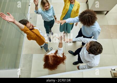 Optimistische, fröhliche Team von fröhlichen Designern, heben die Hände auf, feiern den Sieg im modernen Büro, Blick von oben, Innenaufnahme Stockfoto