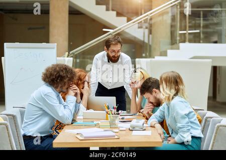 Junge verärgerte Arbeiter hören dem Top-Manager mittleren Alters zu, starren nachdenklich auf Papiere, denken mit unzufriedenem Ausdruck über zukünftige strategische Schritte nach. B Stockfoto