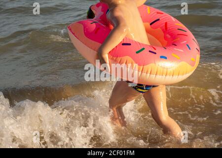 Ein 5-jähriger Junge schwimmt im Meer, freut sich und hat Spaß in einem aufblasbaren Ring in Form eines Donuts. Stockfoto