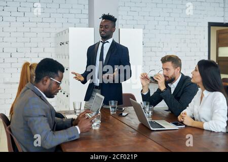 Sympathischer schwarzer Mitarbeiter erklärt ausländischen Kollegen neue Client-Management-Strategie-Idee bei modernen Gruppenbüros Ausbildung Stockfoto