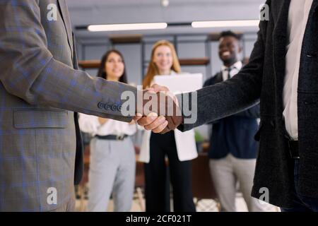 Multi-ethnischen Team nach erfolgreichem Treffen schütteln die Hände zu einander. Afrikanische und kaukasische Führungskräfte in Smoking im Büro Stockfoto