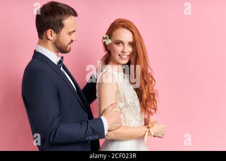 Mann trägt eleganten Anzug scharfsinnig Blick auf Frau mit roten Auburn Haar mit Blume. Bärtiger Mann glätten Haar isoliert über rosa Hintergrund Stockfoto